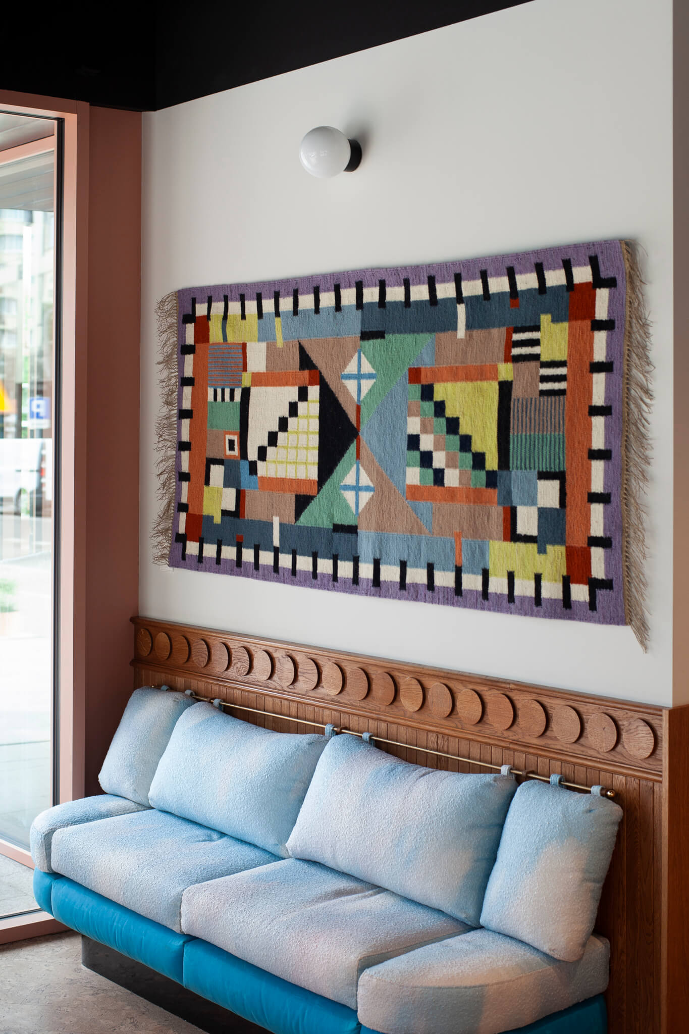 Colorful geometric tapestry hanging above a blue sofa in a modern living room. Designed by Piotr Niklas for Splot via Ad Origine.
